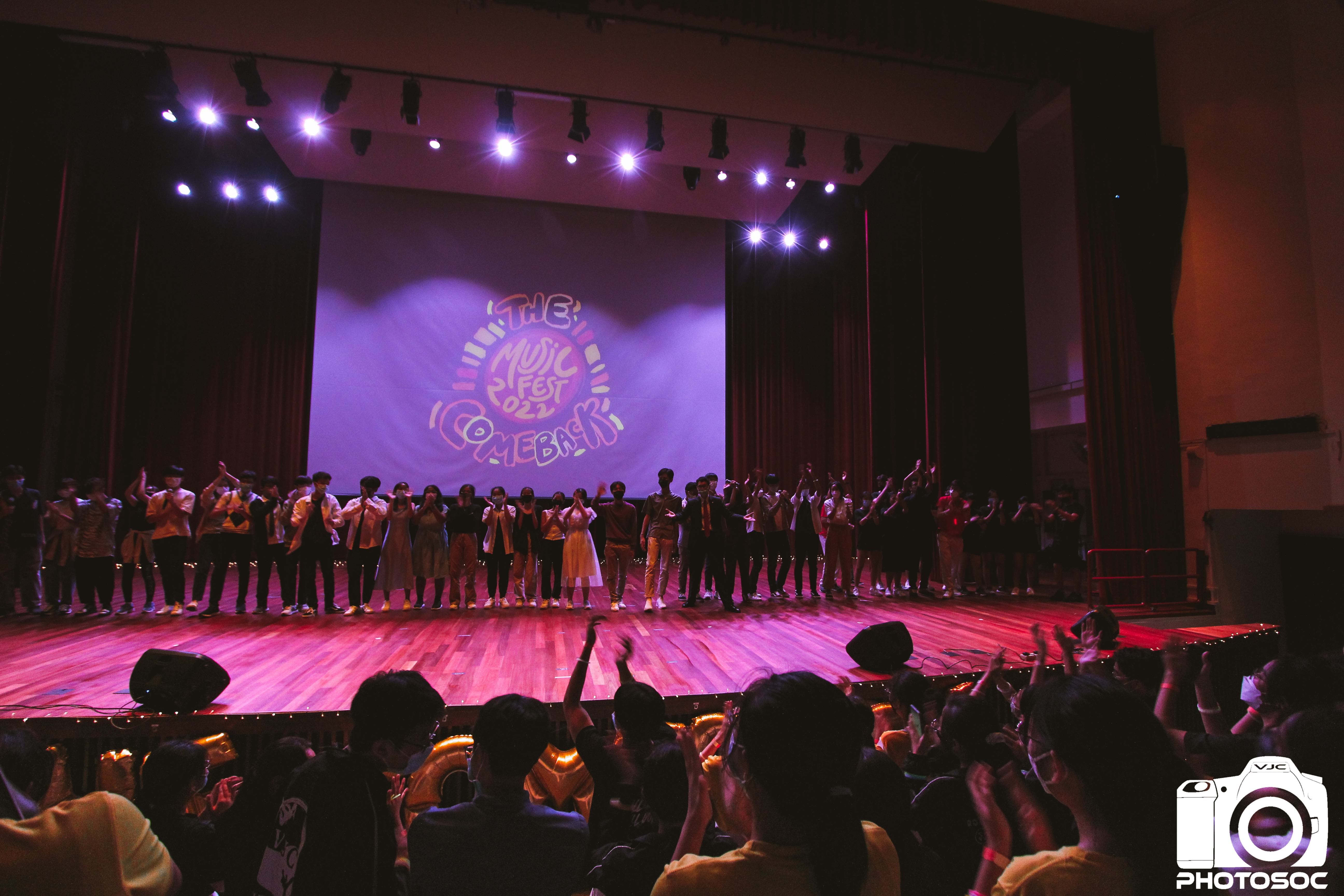 A large group of performers stands on a lit stage at The Music Fest 2022 Comeback event, facing an applauding audience.